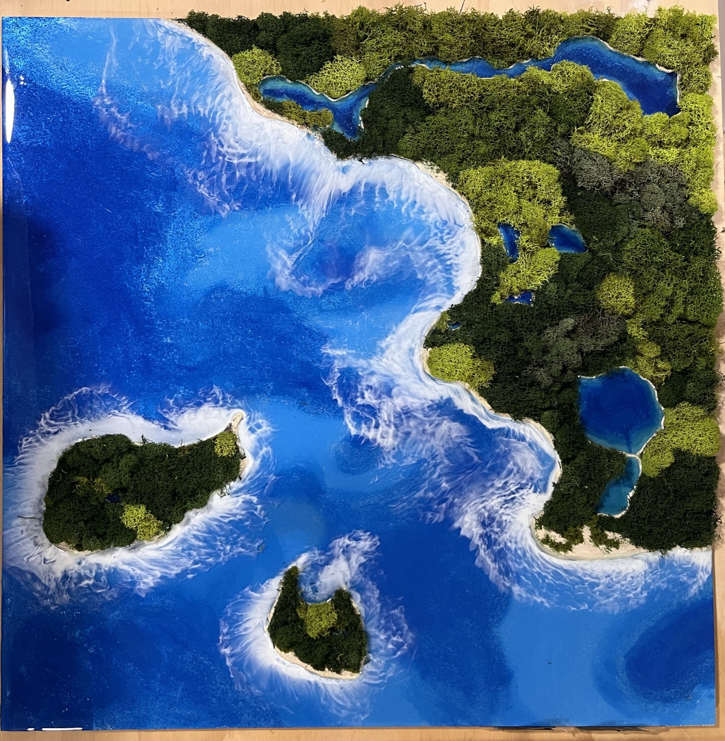 Aerial lake artwork with dramatic white waves in blue epoxy resin and green moss